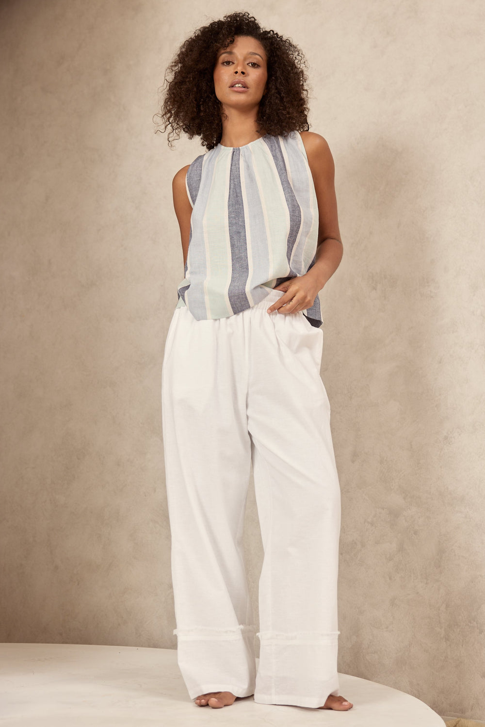 Woman wearing a sleeveless striped top and white pants against a beige background