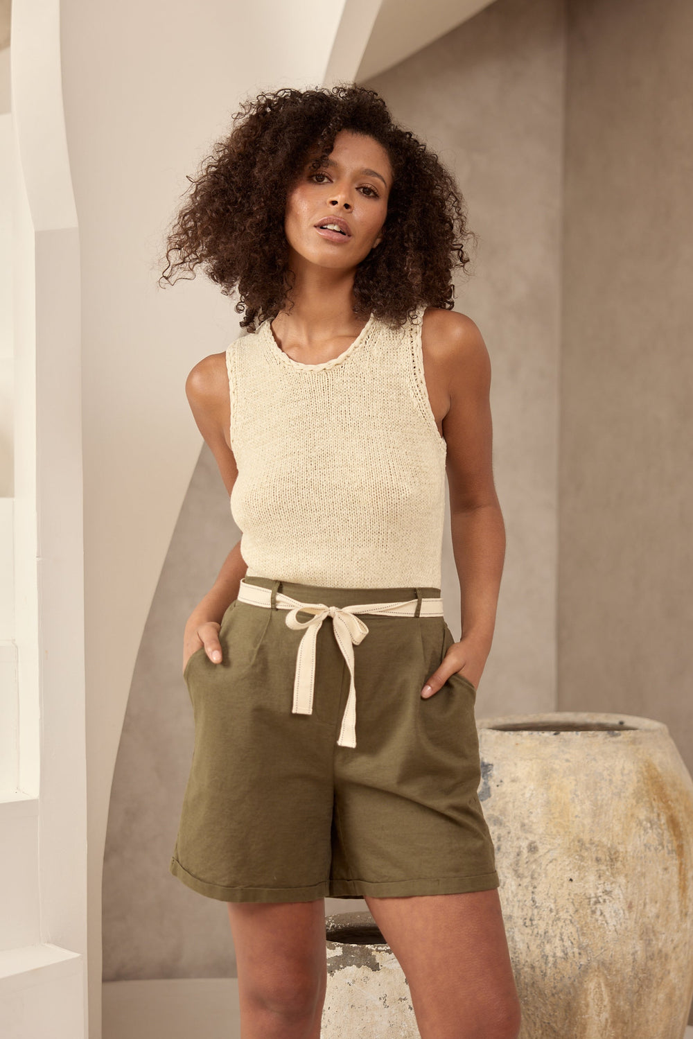 Woman wearing a sleeveless top and khaki shorts standing in a neutral setting