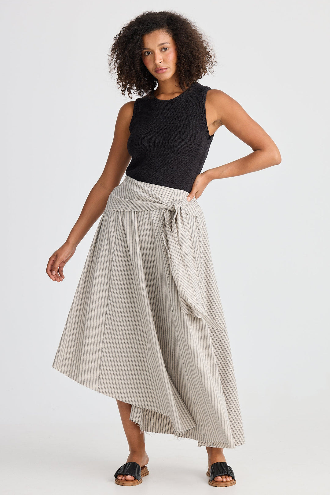 Woman wearing a black sleeveless top and striped skirt on a white background