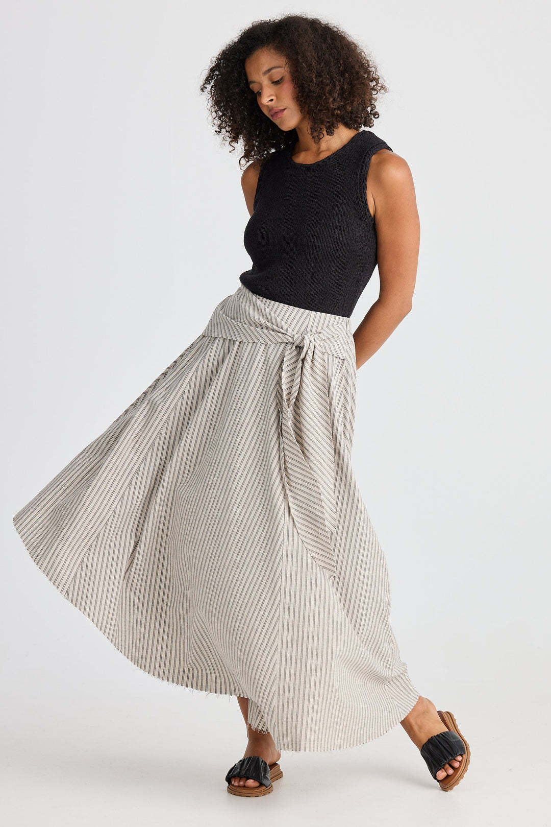 Woman wearing a black sleeveless top and striped skirt on a white background