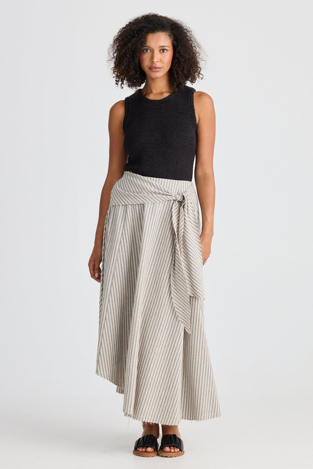 Woman wearing a black sleeveless top and striped skirt on a white background