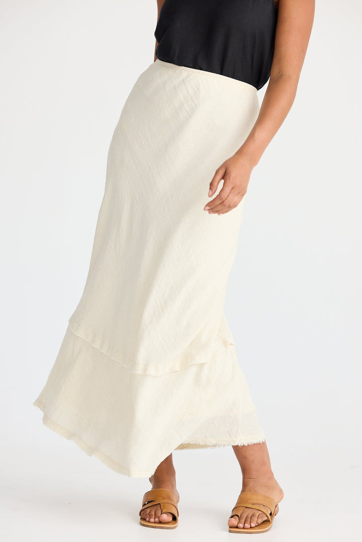 Person wearing a cream skirt and black top on a white background