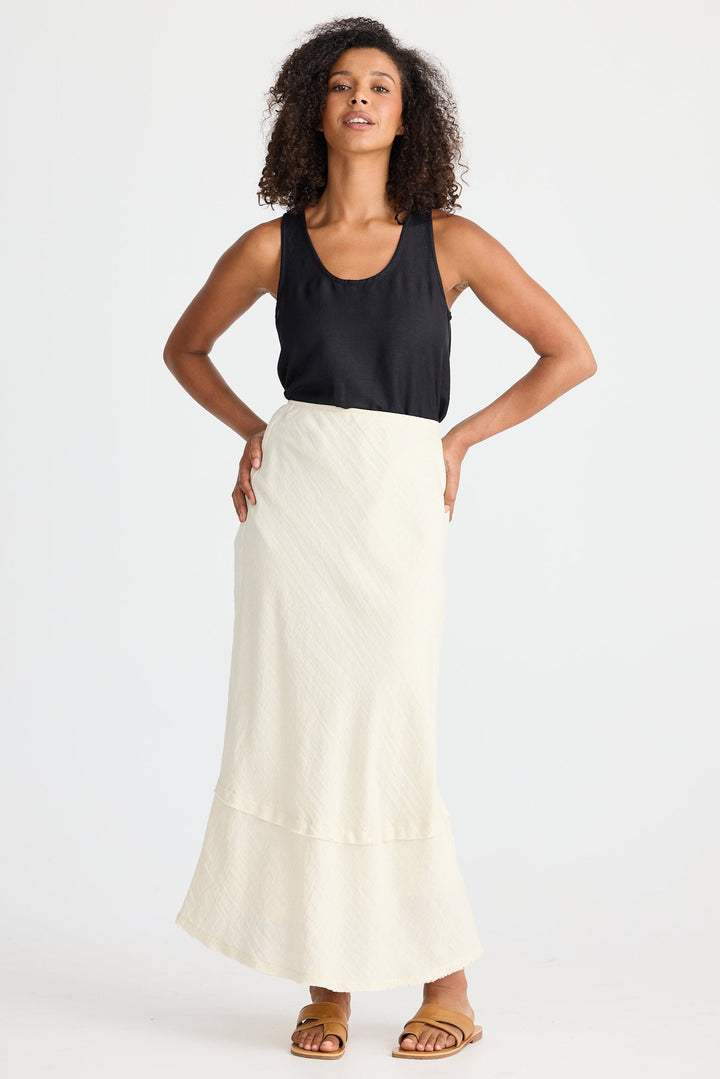 Woman wearing a black sleeveless top and cream skirt on a white background
