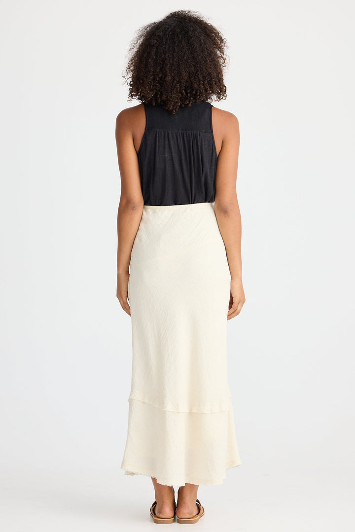 Person wearing a black top and cream skirt on a white background