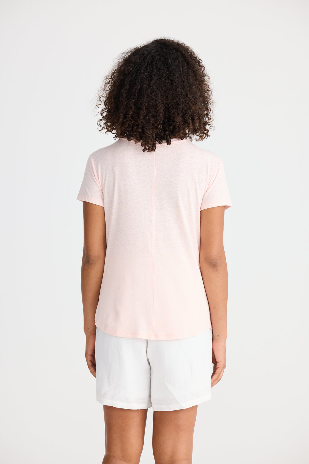 Person wearing a light pink t-shirt and white shorts on a plain background