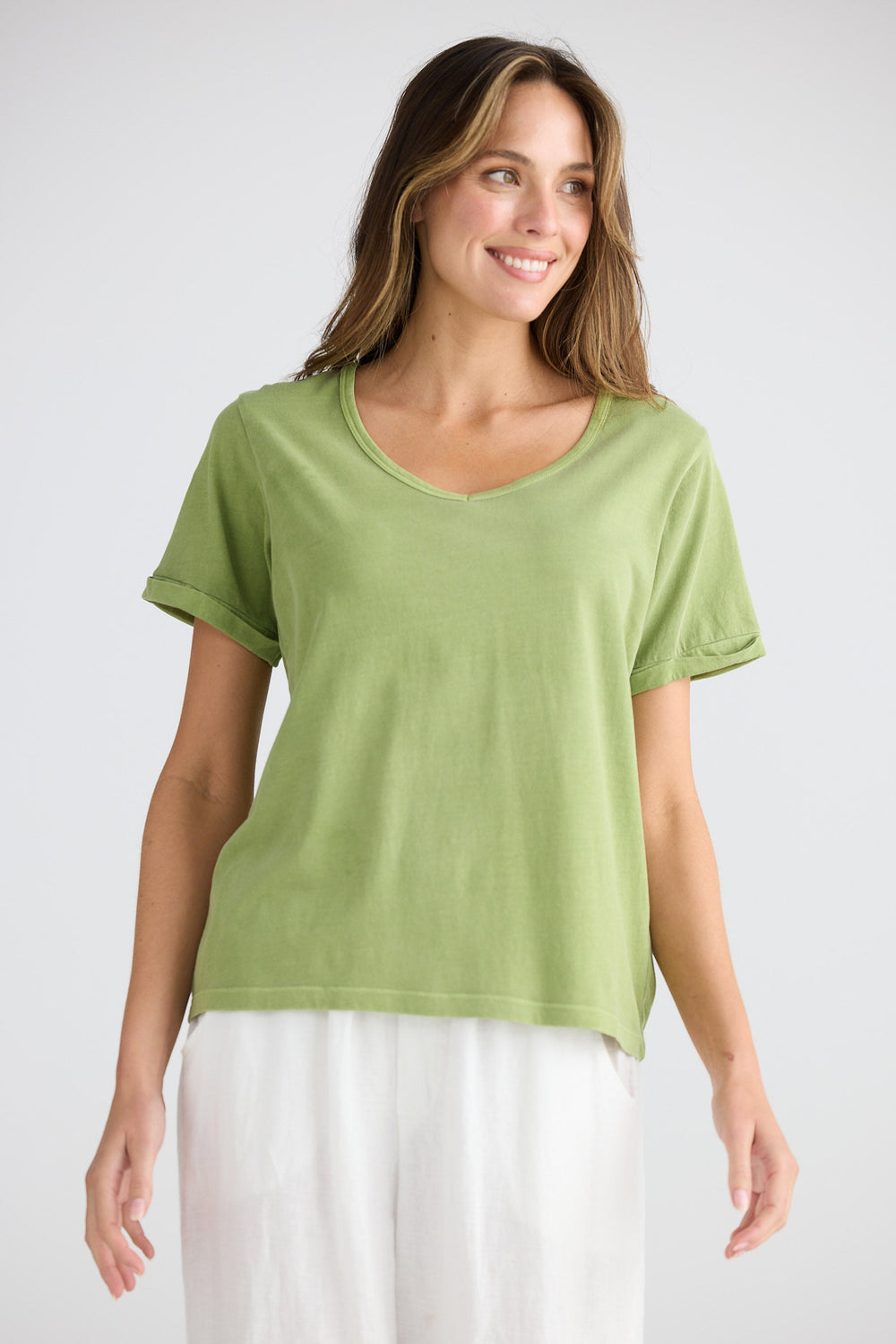 Woman wearing a green t-shirt and white pants on a plain background