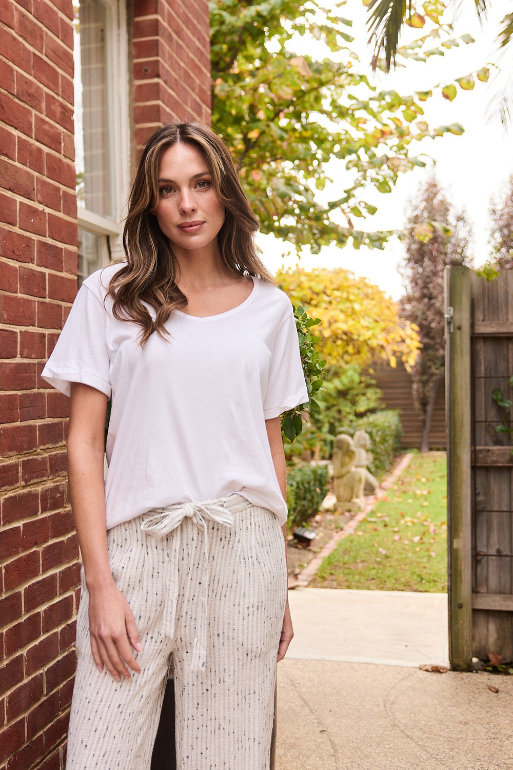 Woman standing outdoors next to a brick wall with a garden in the background
