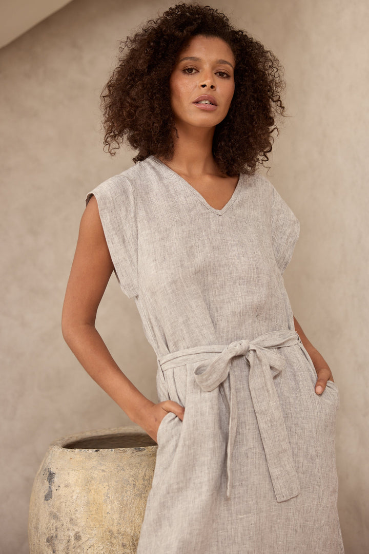 Woman wearing a light gray sleeveless dress with a belt against a neutral background