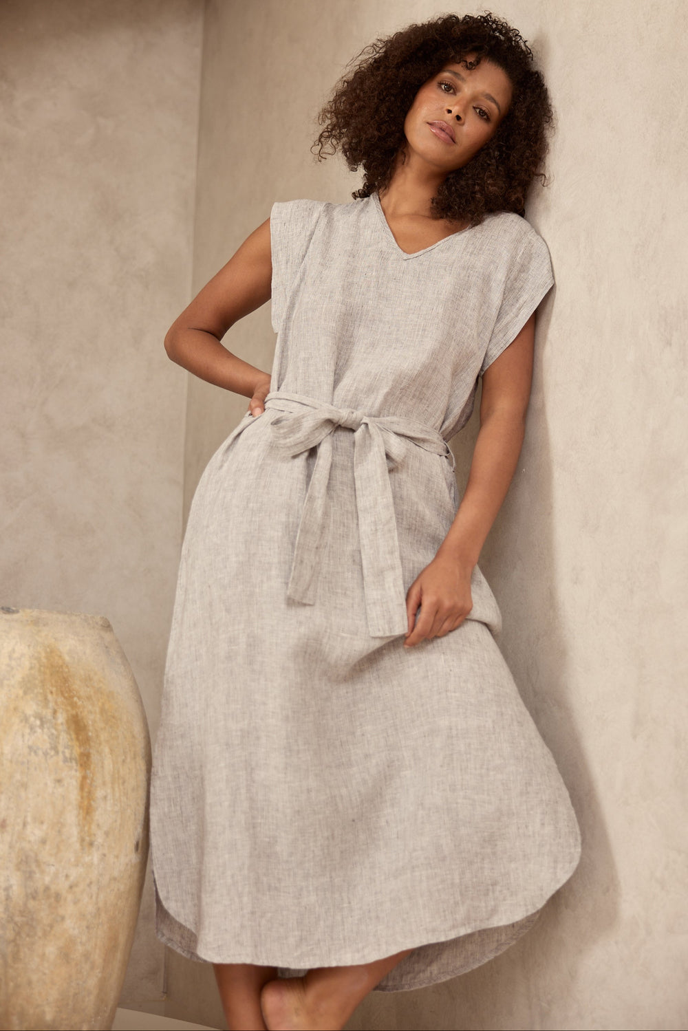 Woman wearing a light gray dress against a textured beige wall.