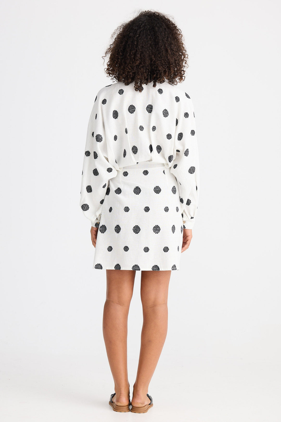 Person wearing a white dress with black polka dots from behind on a white background