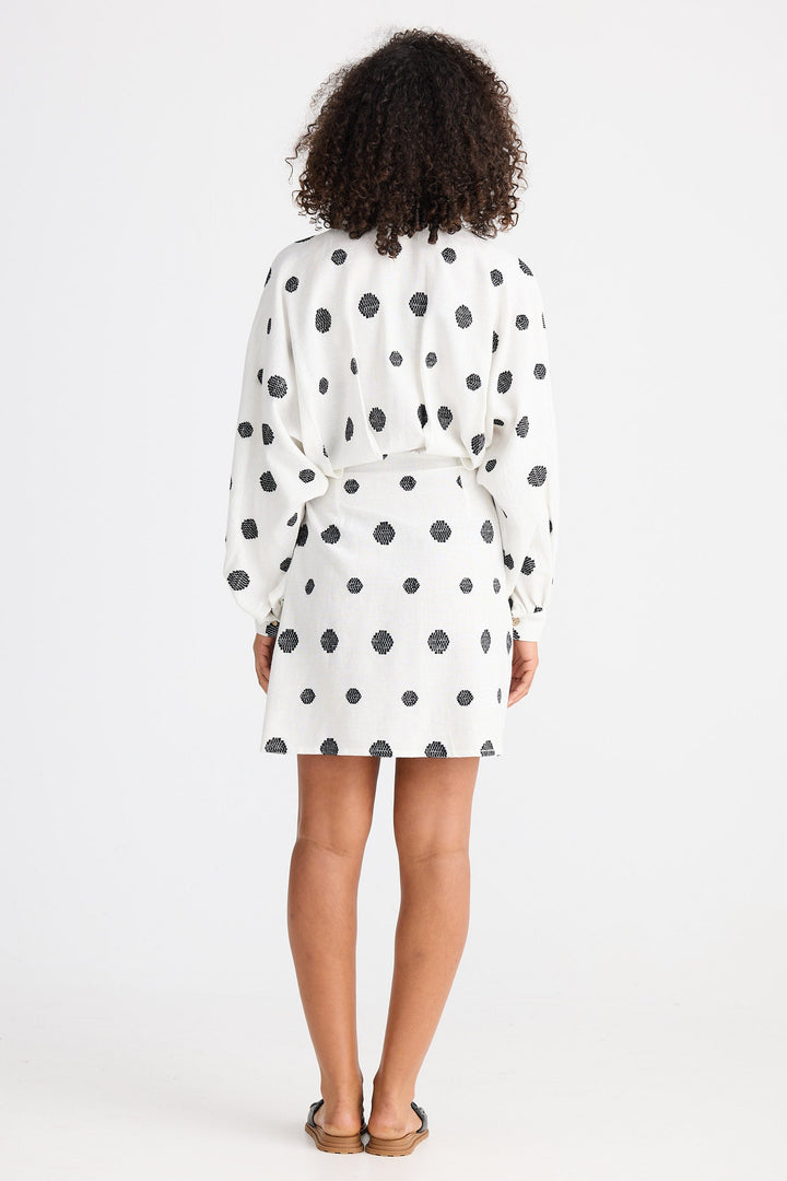 Person wearing a white dress with black polka dots from behind on a white background