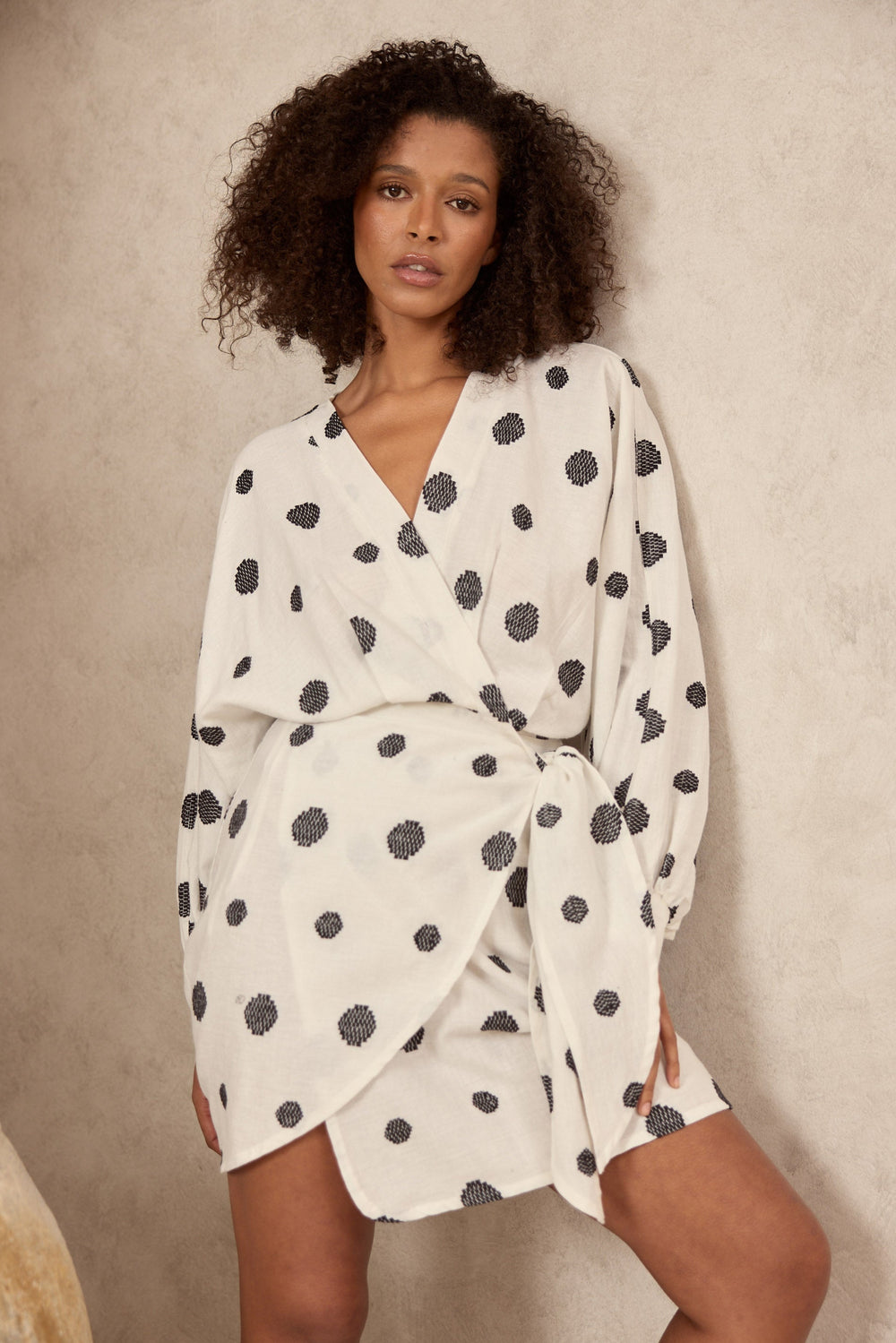 Woman wearing a white dress with black polka dots against a beige background
