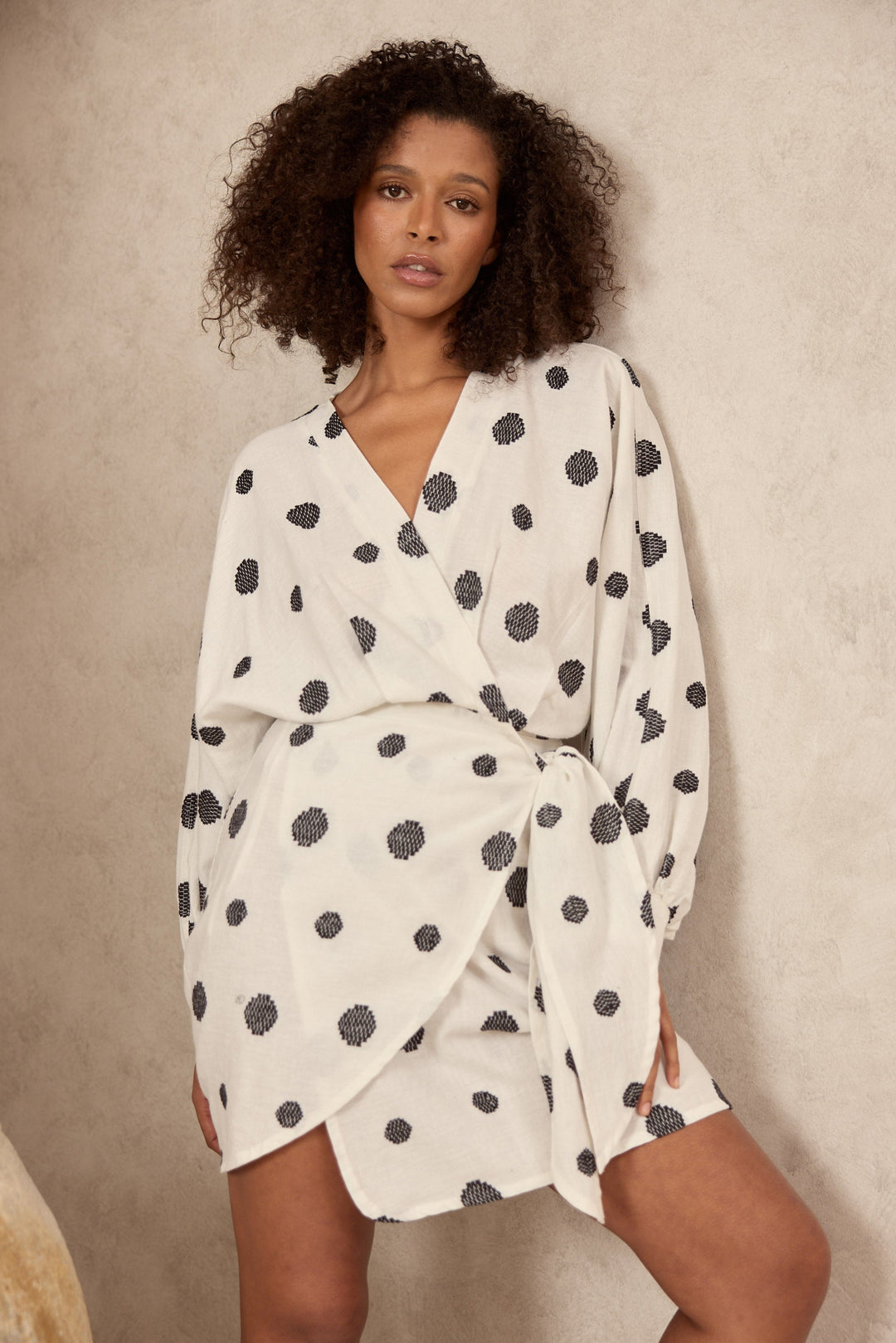 Woman wearing a white dress with black polka dots against a beige background