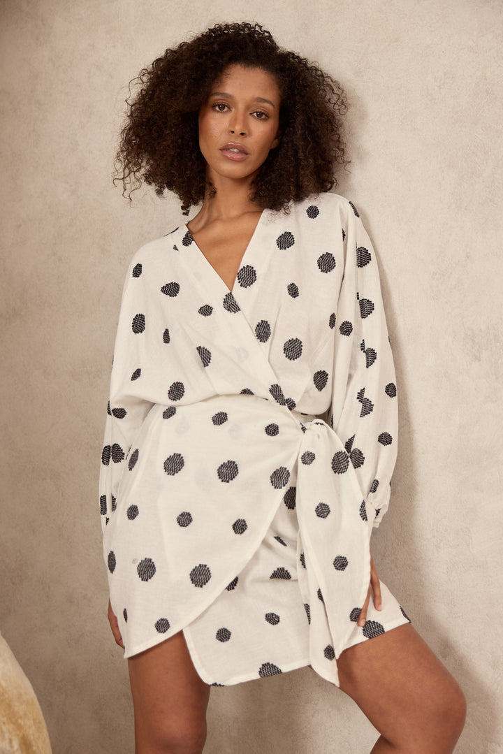 Woman wearing a white dress with black polka dots against a beige background