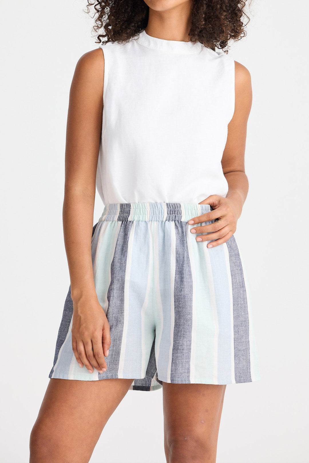 Woman wearing a white sleeveless top and striped shorts on a plain background