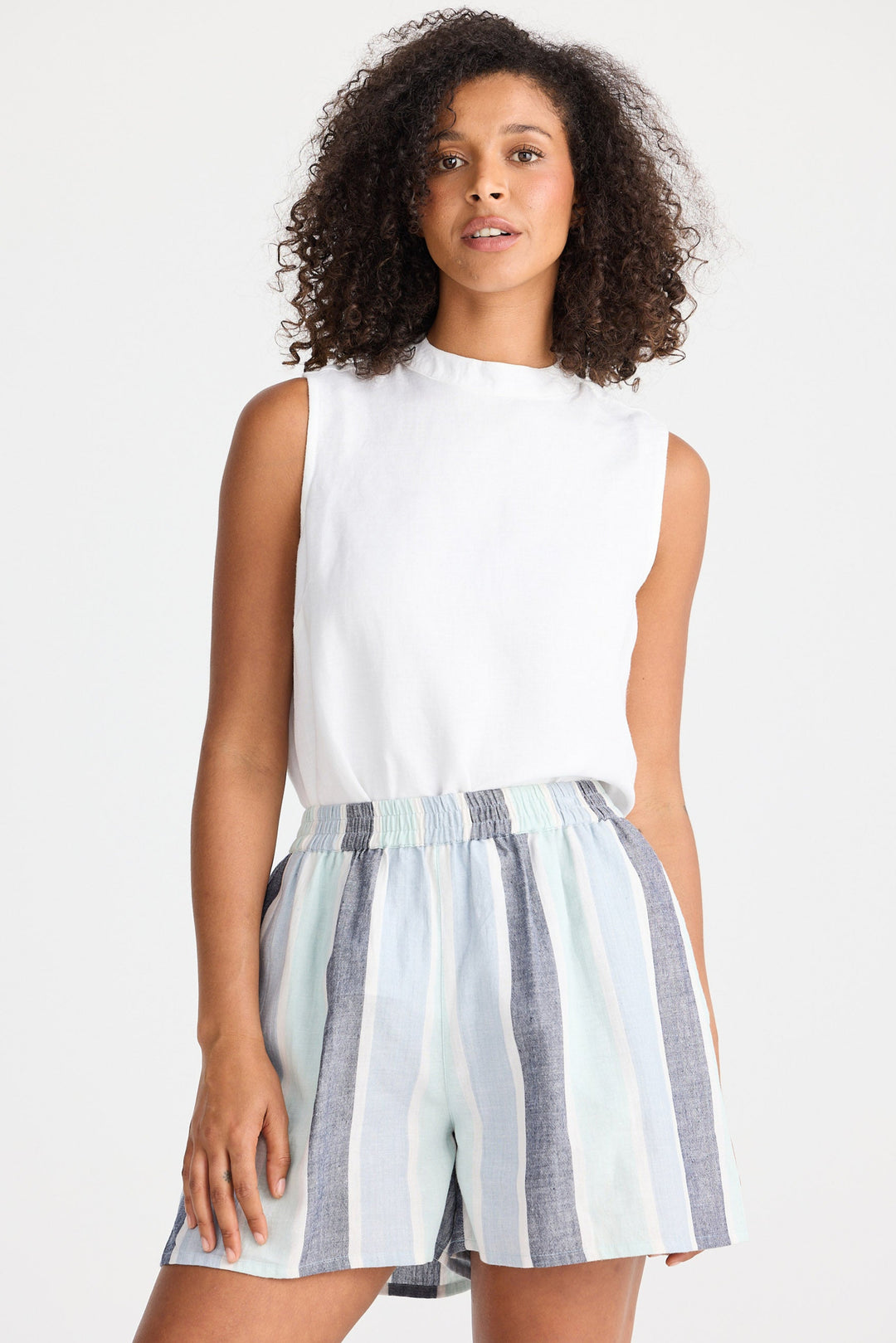Woman wearing a white sleeveless top and striped shorts on a plain background