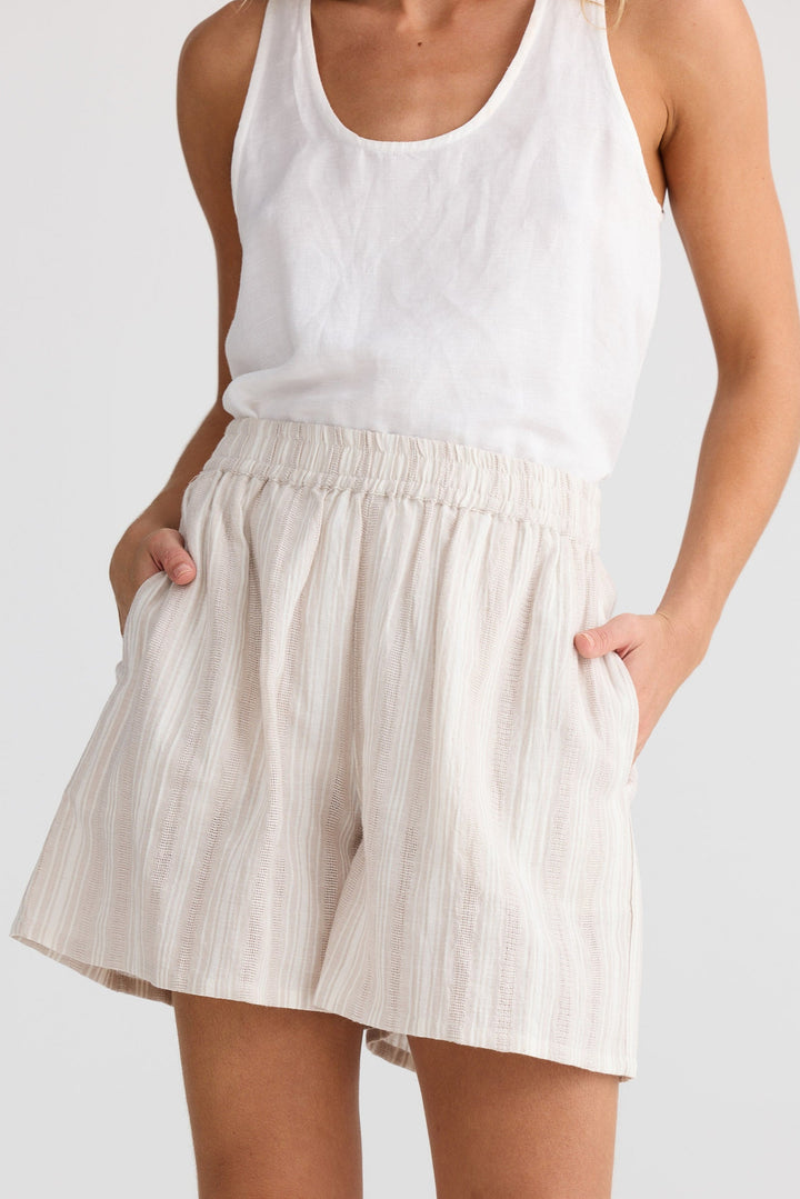Person wearing a white tank top and beige shorts on a plain background