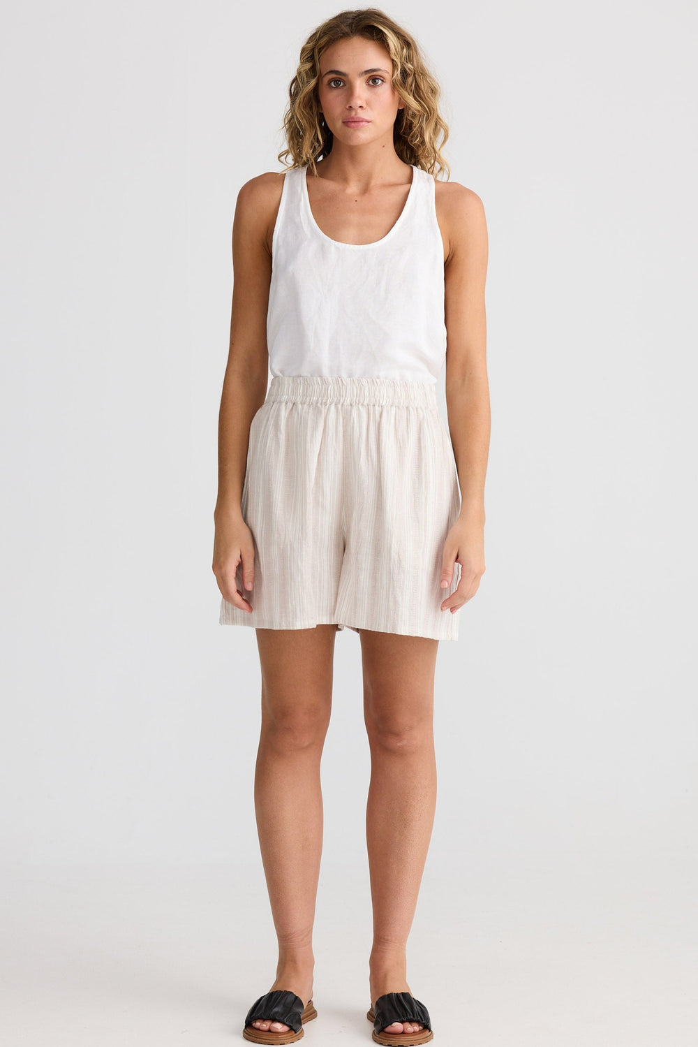 Woman wearing a white tank top and beige shorts on a white background