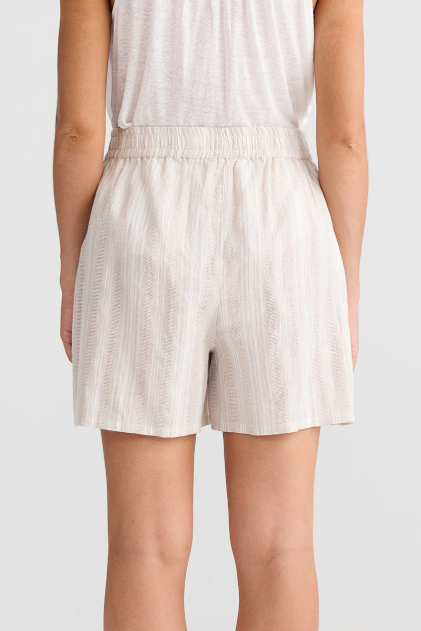 Woman wearing a white sleeveless top and shorts set on a plain background