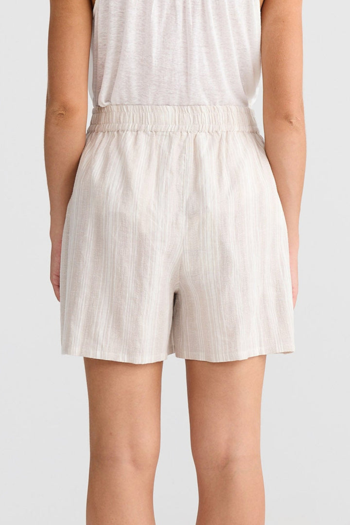 Woman wearing a white sleeveless top and shorts set on a plain background