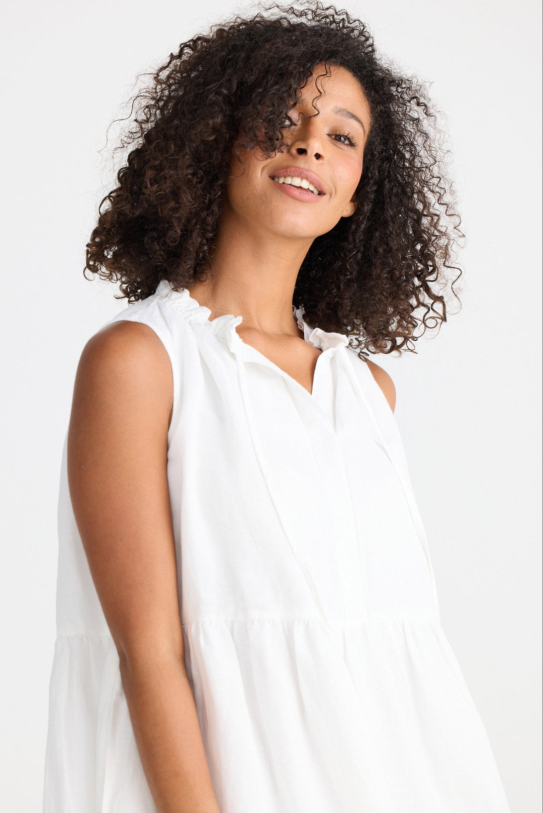 Woman wearing a white sleeveless dress against a plain background