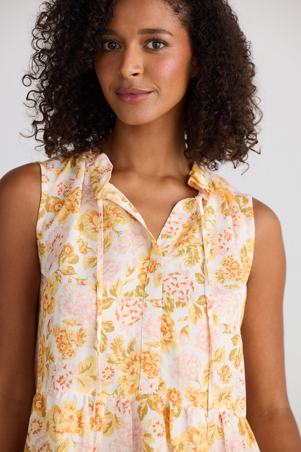 Woman wearing a sleeveless floral dress against a plain background