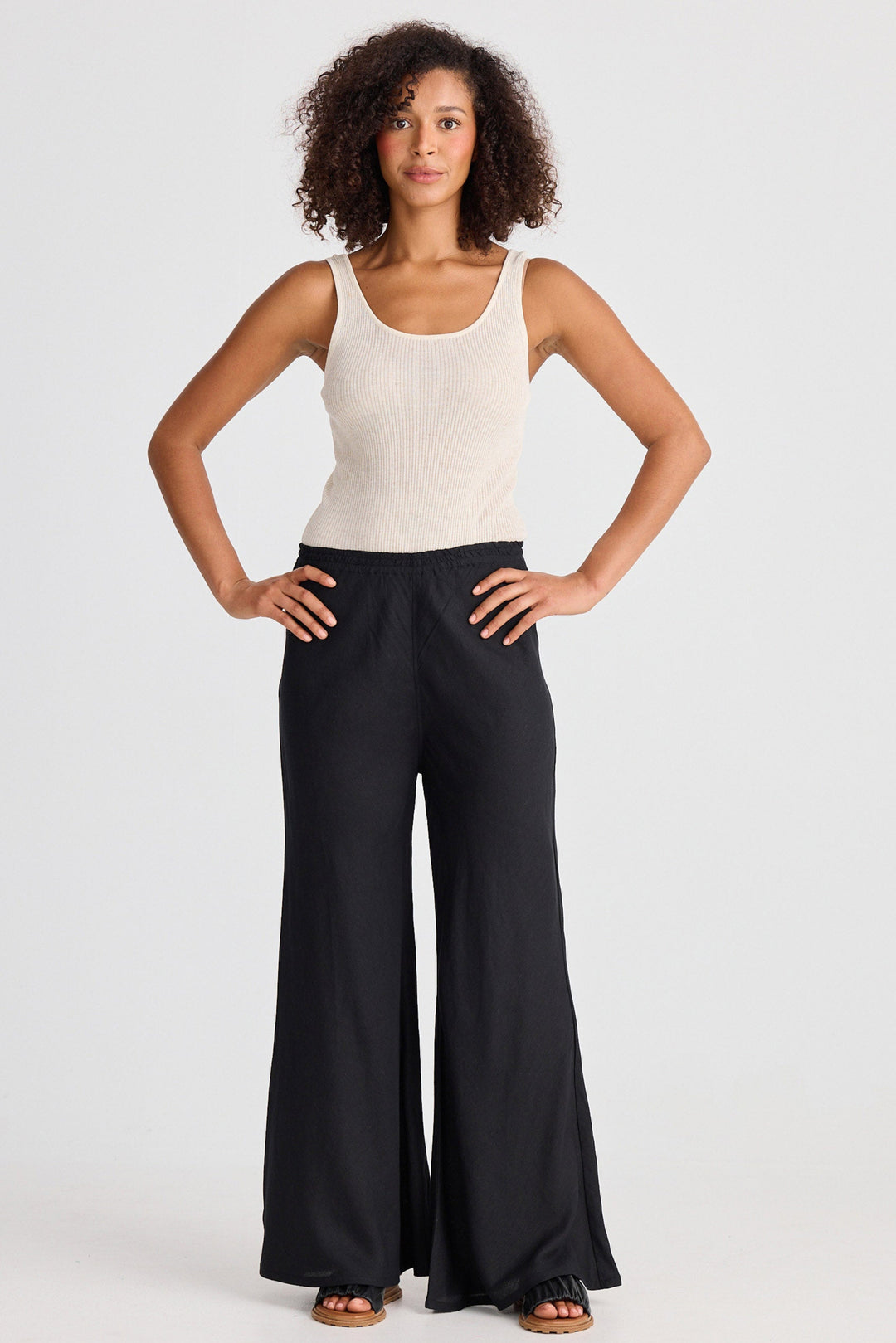 Woman wearing a white tank top and black flared wide-leg pants on a white background