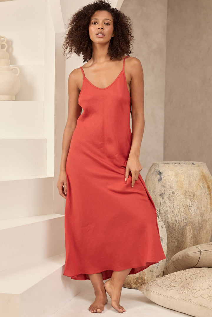 Woman in a red slip dress standing in a modern interior setting with neutral tones.