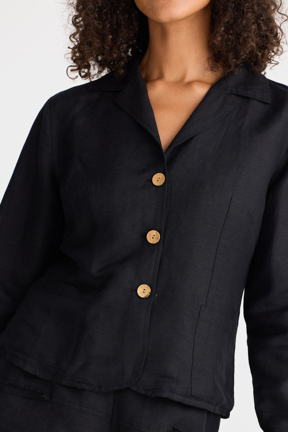 Woman wearing a black jacket with wooden buttons and black pants on a white background