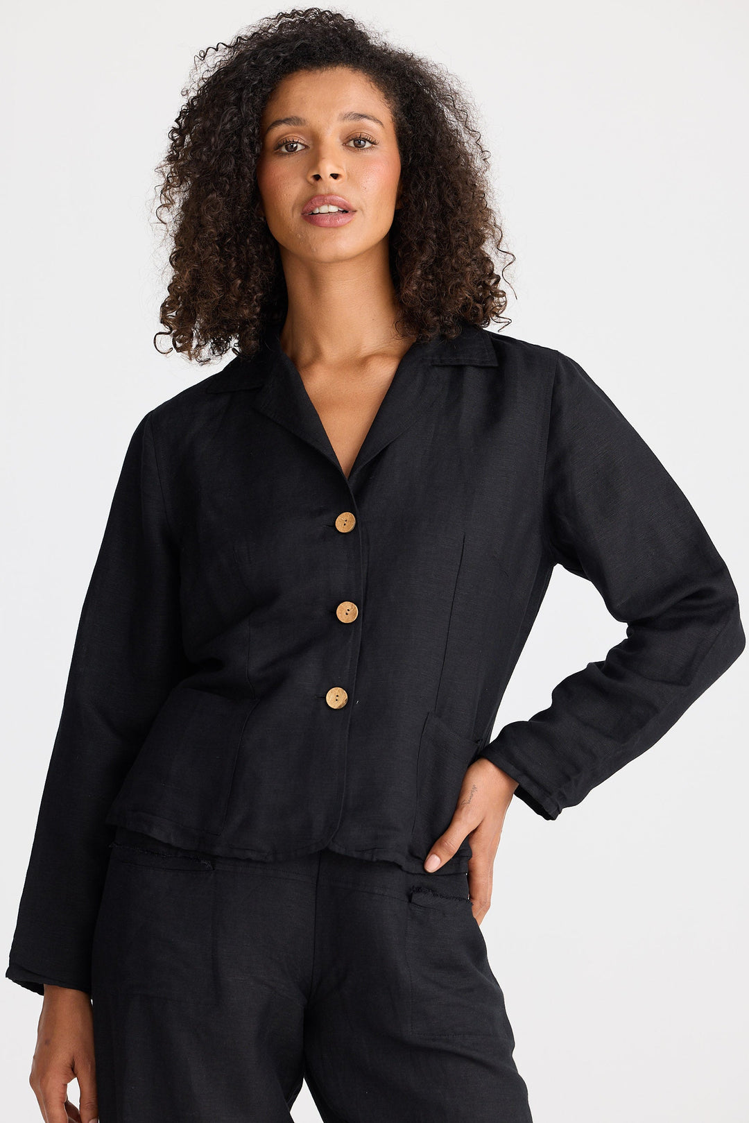 Woman wearing a black jacket with wooden buttons and black pants on a white background