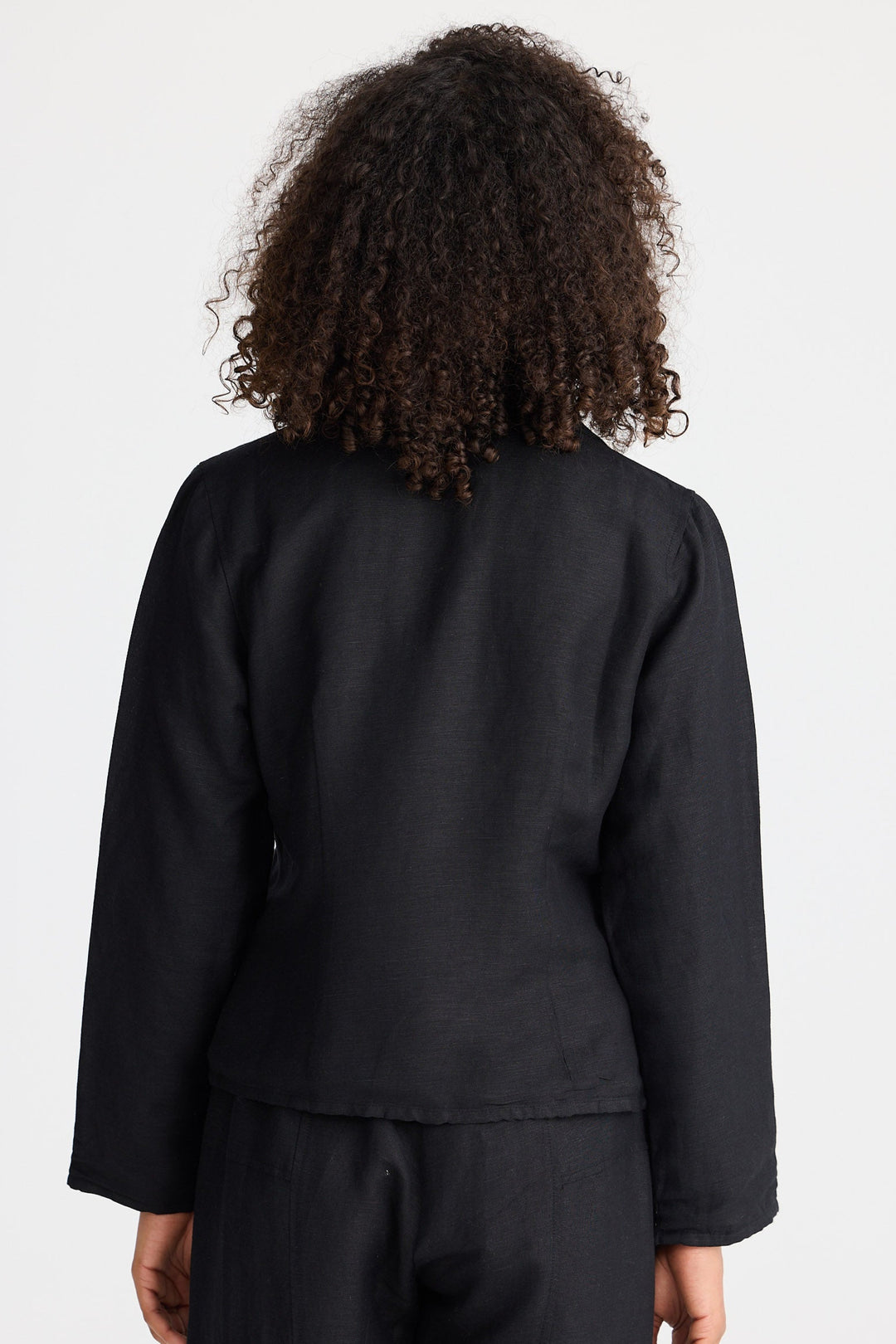 Person wearing a black jacket and pants with a plain background