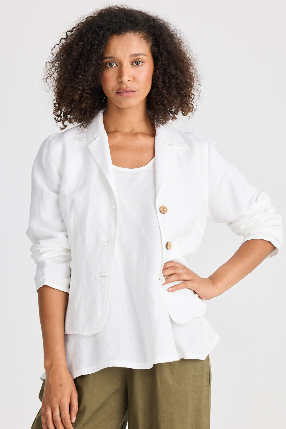 Woman wearing a white jacket over a white shirt with green pants on a plain background