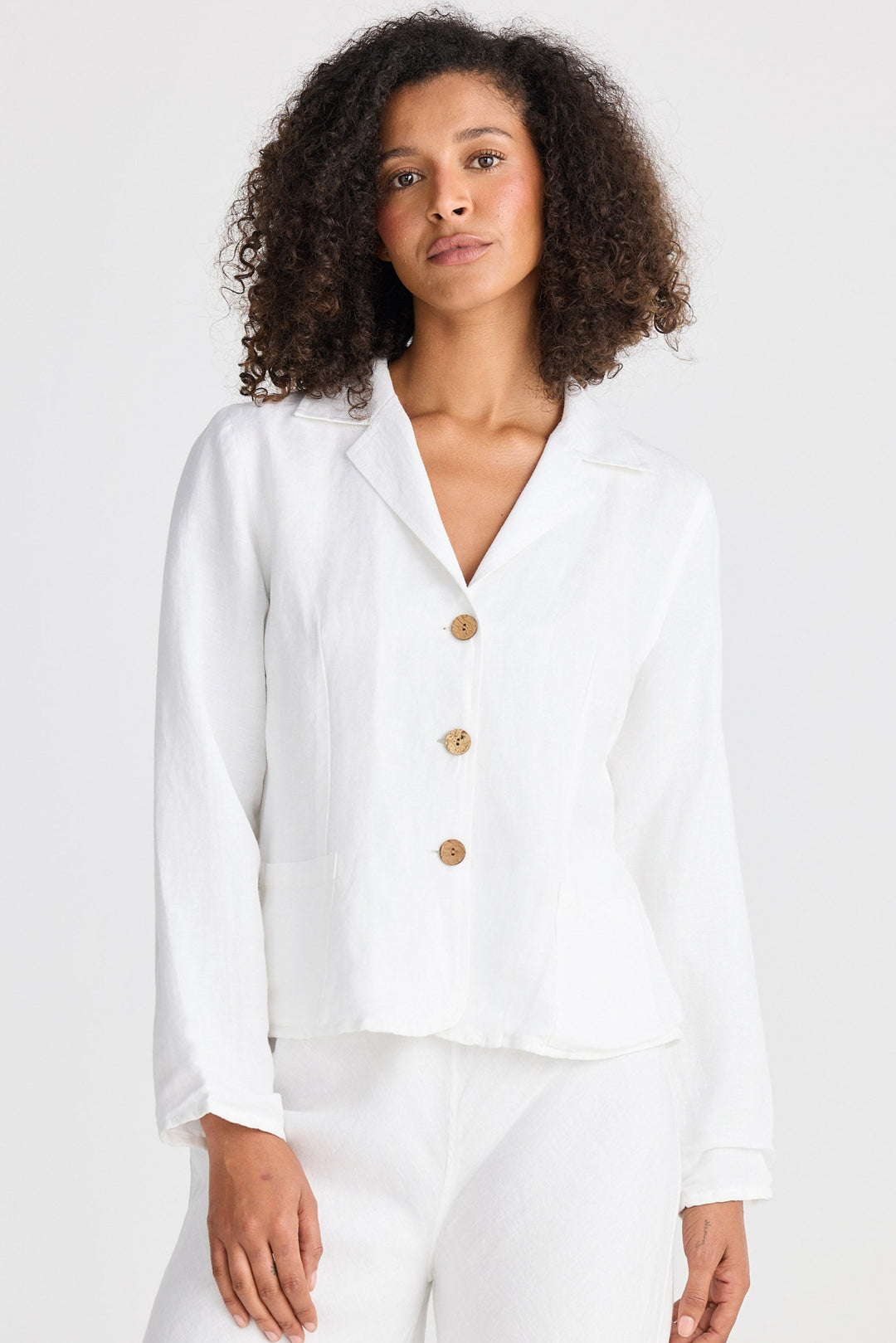Woman wearing a white blazer with wooden buttons on a white background
