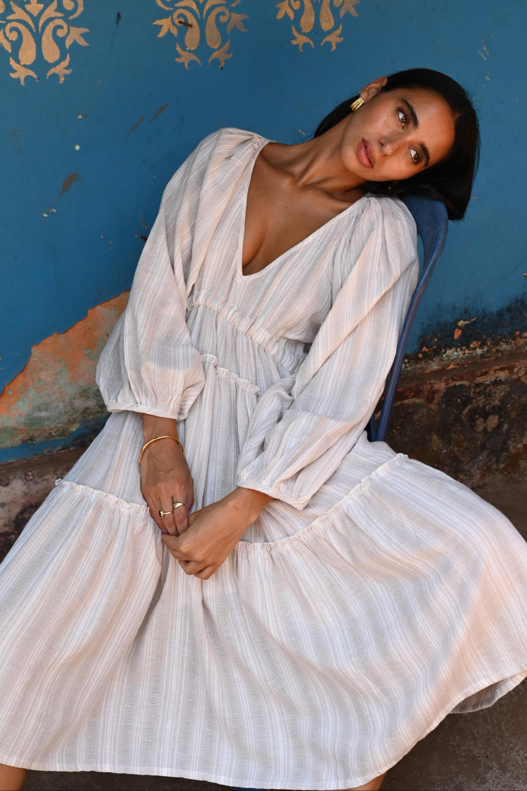 Woman in a light dress sitting in front a blue wall with decorative patterns