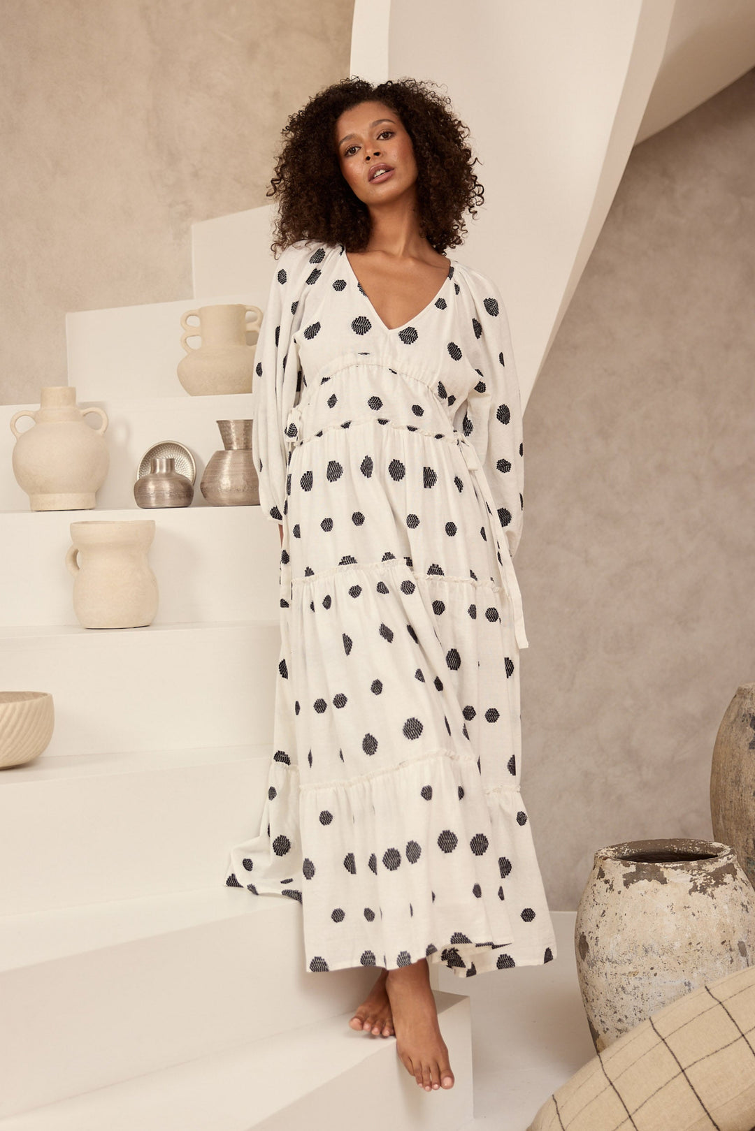 Woman in a polka dot dress standing on a staircase with decorative vases and pots.