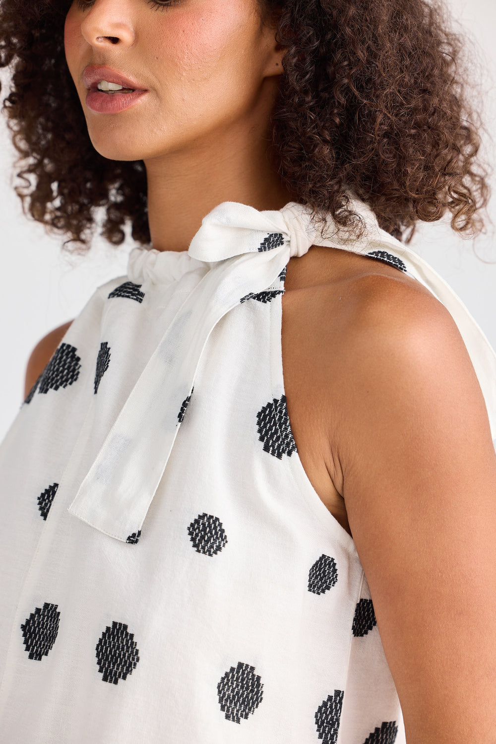 Woman wearing a white sleeveless top with black polka dots