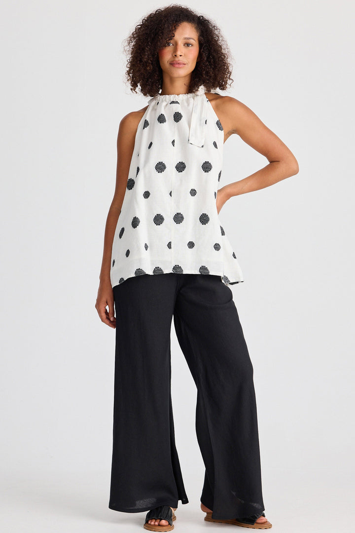 Woman wearing a white sleeveless top with black polka dots and black pants on a white background