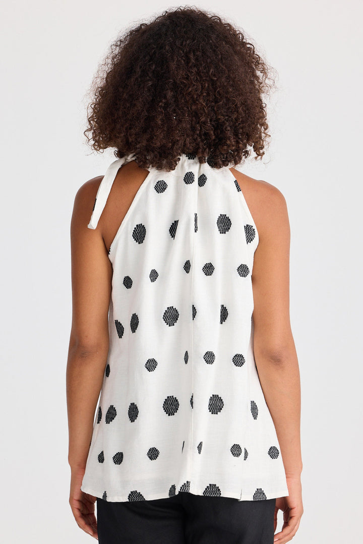 Woman wearing a white sleeveless top with black polka dots and black pants on a white background