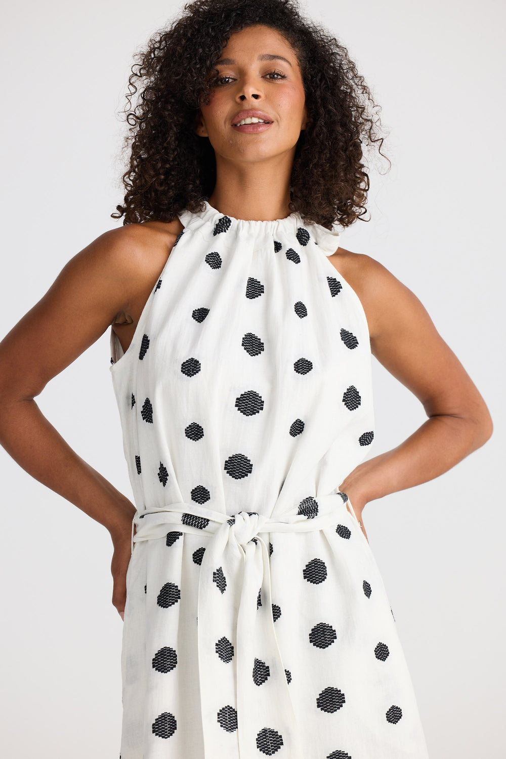 Woman wearing a white dress with black polka dots against a plain background