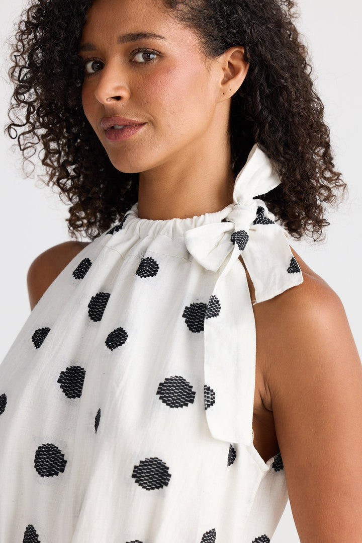 Woman wearing a white dress with black polka dots against a plain background