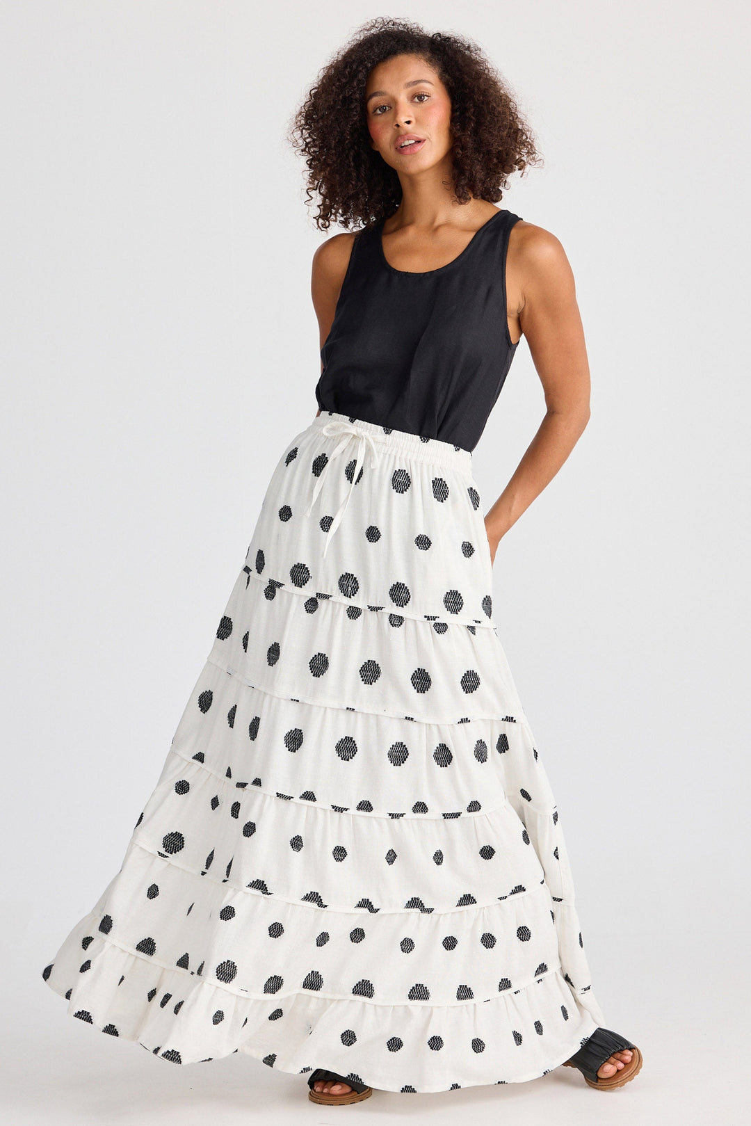 Woman wearing a black sleeveless top and white skirt with black polka dots on a white background