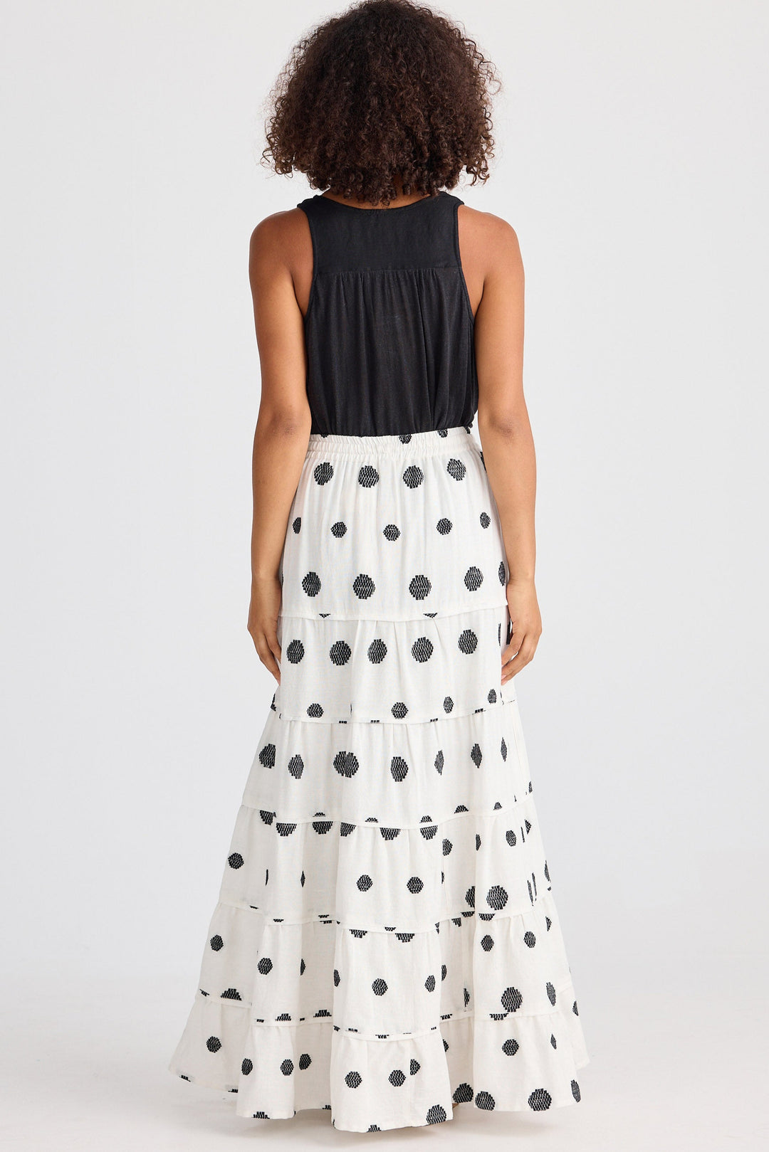 Woman wearing a black sleeveless top and white polka dot skirt on a white background