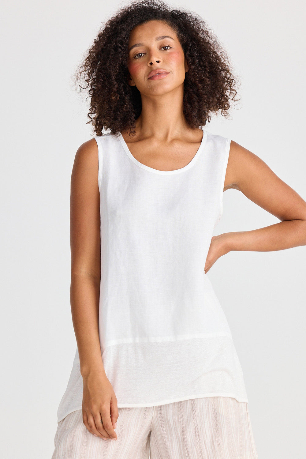 Woman wearing a white sleeveless top and light-colored shorts on a plain background