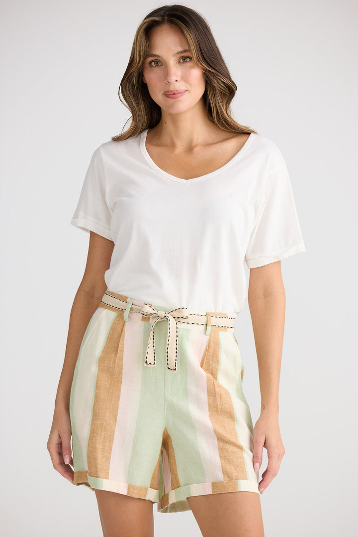 Woman wearing a white top and colorful striped shorts on a plain background