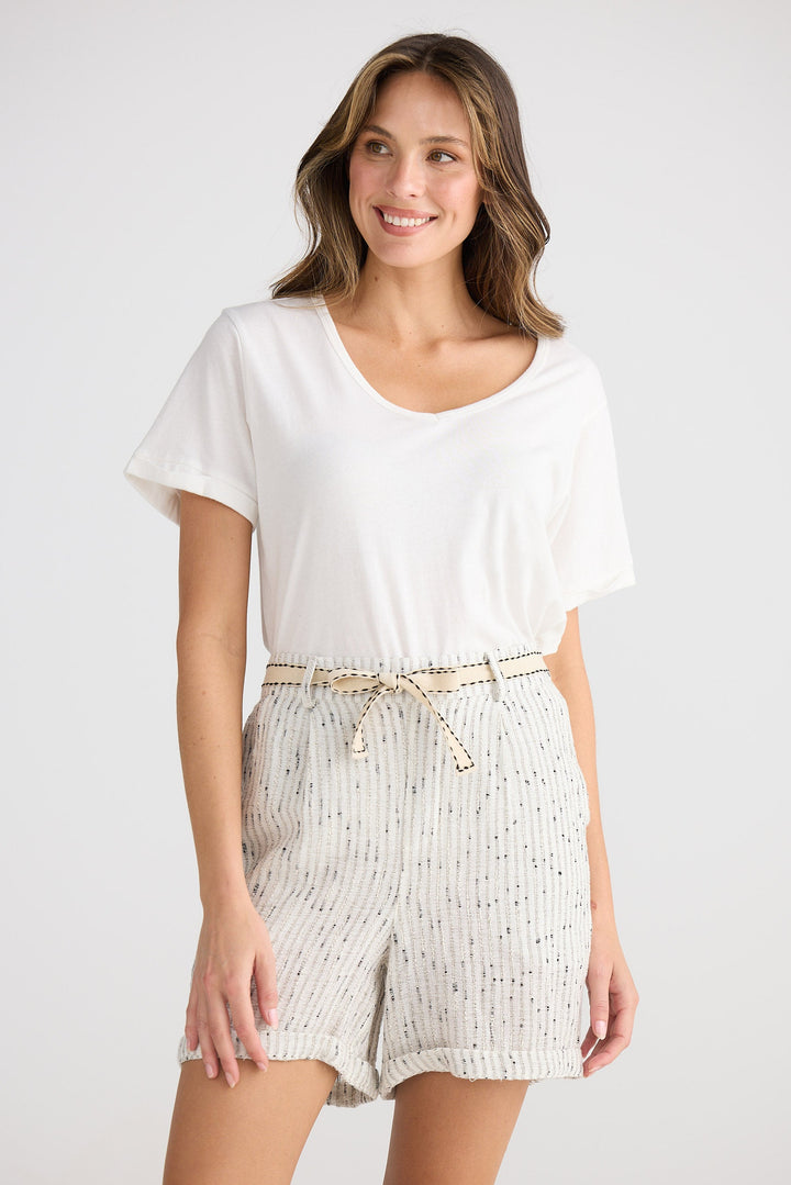 Woman wearing a white top and striped shorts on a plain background