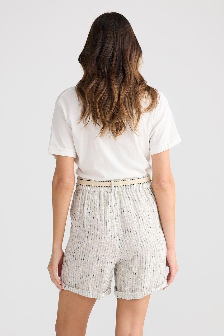 Woman wearing a white t-shirt and light-colored shorts on a plain background