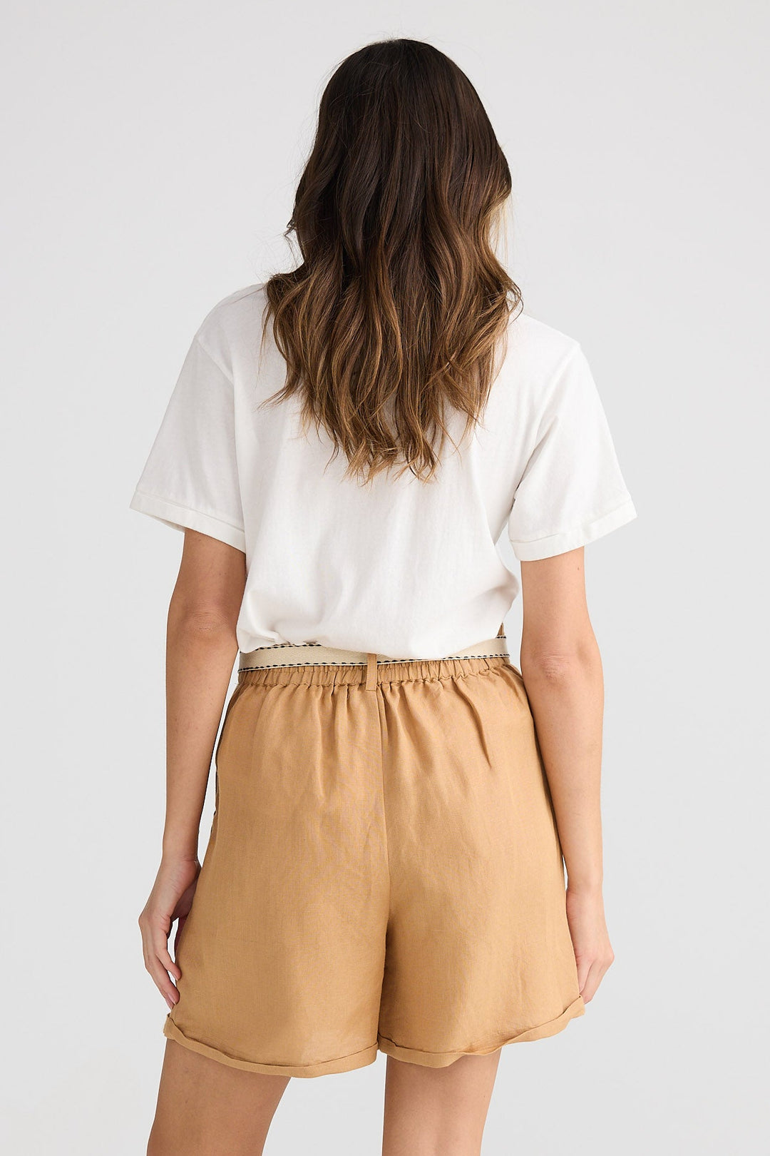 Woman wearing beige shorts and a white top on a plain background