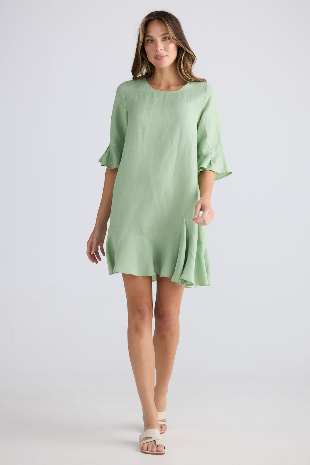 Woman wearing a light green dress with ruffled sleeves on a white background