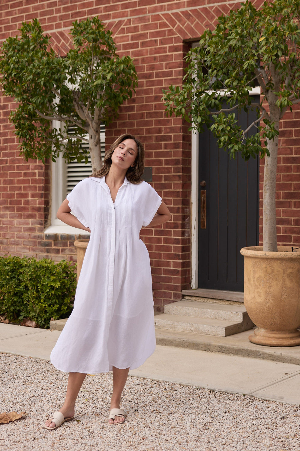 Woman in a white dress standing in front of a brick building with greenery.