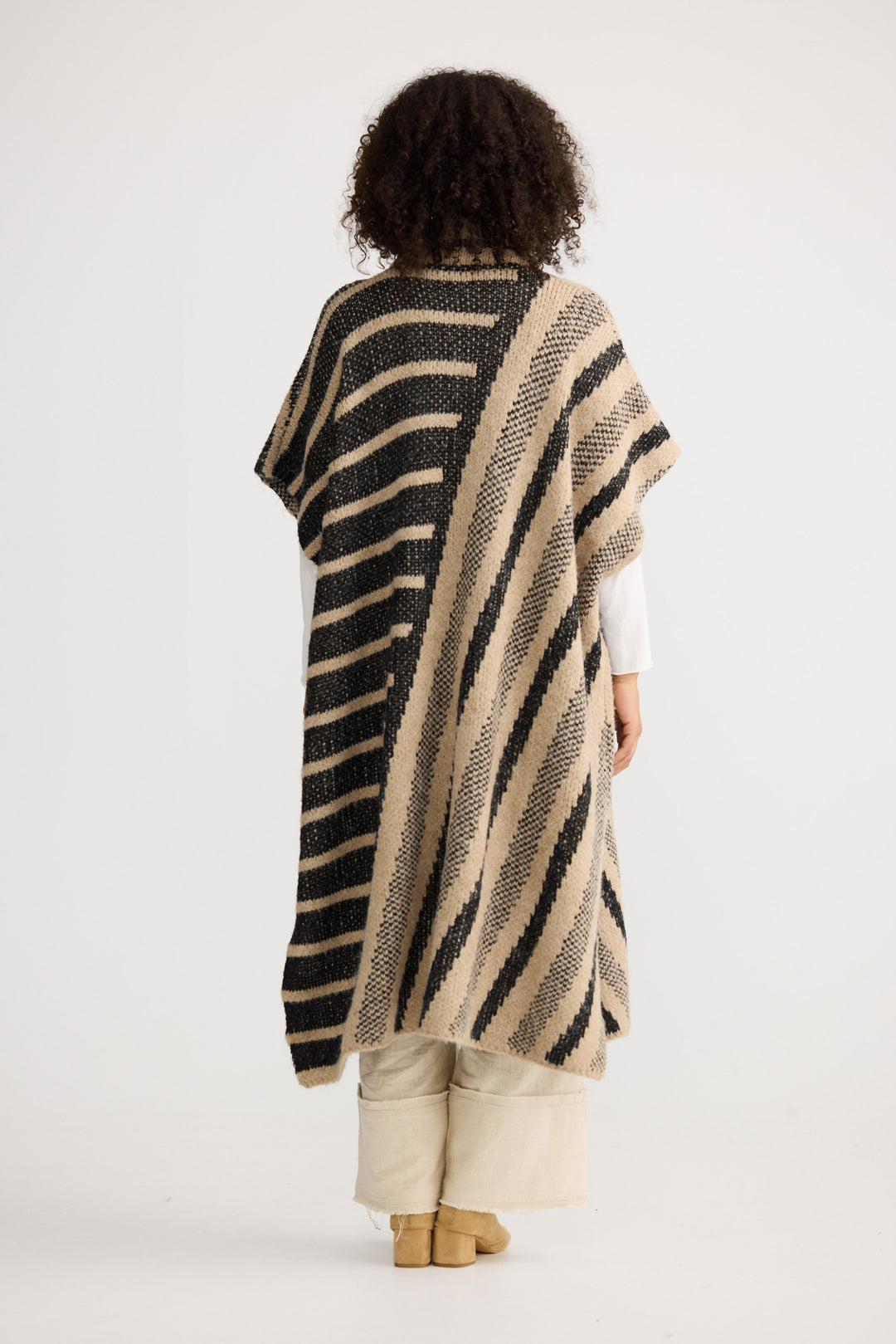 Model wearing black w cedar stripe Mirador Knit Cape, back view on white background